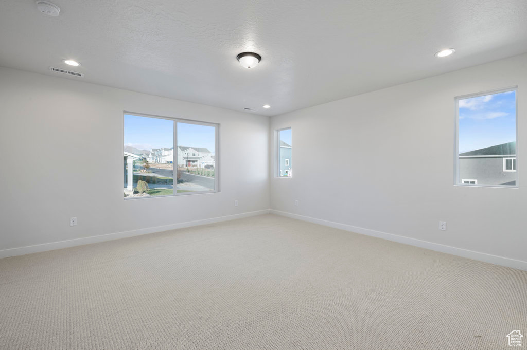 Empty room with baseboards, recessed lighting, visible vents, and light carpet
