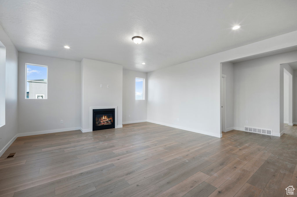 Unfurnished living room featuring plenty of natural light, baseboards, a glass covered fireplace, and wood finished floors
