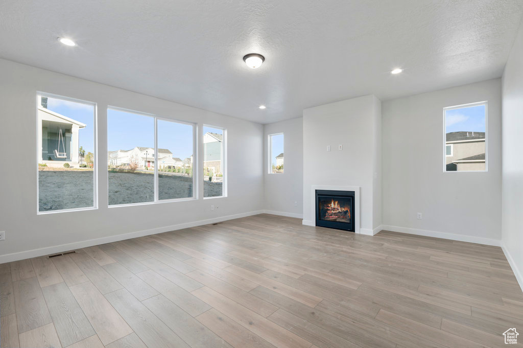 Unfurnished living room featuring baseboards, a glass covered fireplace, visible vents, and light wood-style floors