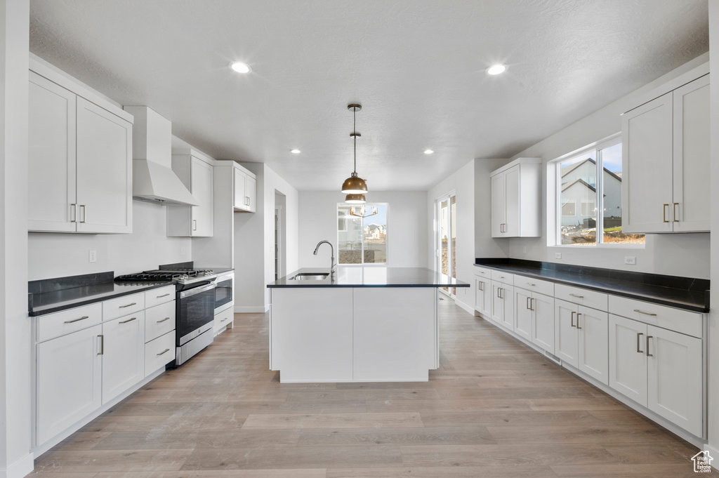 Kitchen with white cabinets, dark countertops, a sink, stainless steel gas stove, and custom exhaust hood