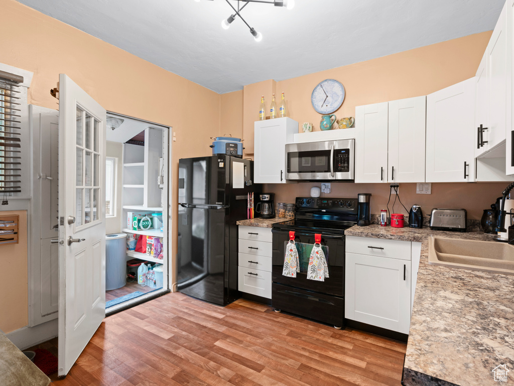 Kitchen featuring white cabinets, a sink, black appliances, and light wood-type flooring