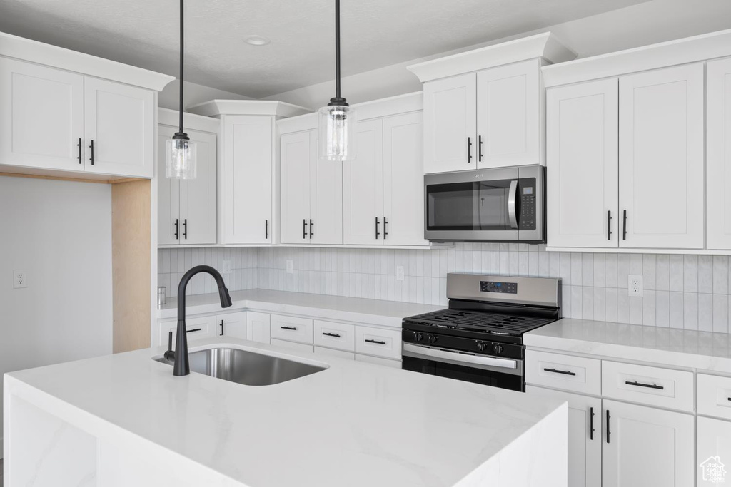 Kitchen featuring a sink, light countertops, stainless steel appliances, white cabinetry, and tasteful backsplash