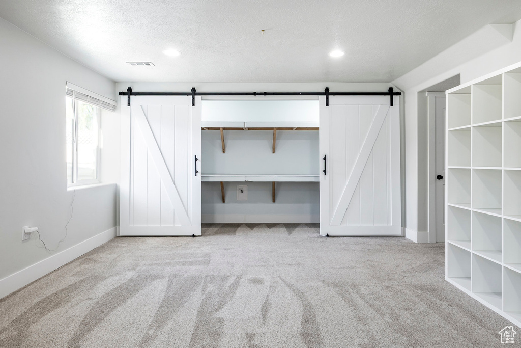Unfurnished bedroom with a barn door, a textured ceiling, carpet, recessed lighting, and baseboards