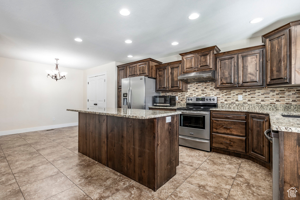 Kitchen with an inviting chandelier, dark brown cabinetry, under cabinet range hood, tasteful backsplash, and appliances with stainless steel finishes