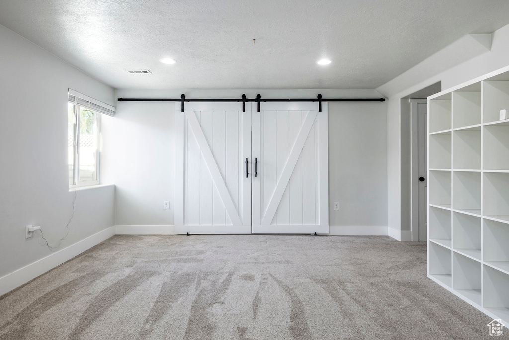 Unfurnished bedroom with a textured ceiling, carpet flooring, and a barn door