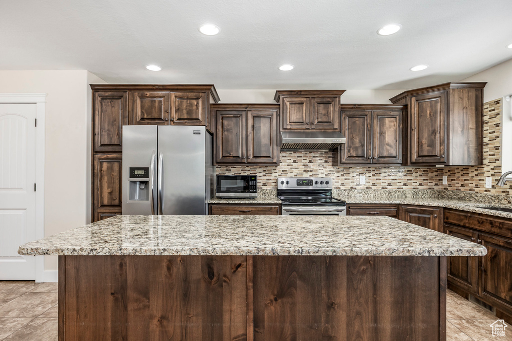 Kitchen featuring a kitchen island, dark brown cabinets, under cabinet range hood, backsplash, and stainless steel appliances