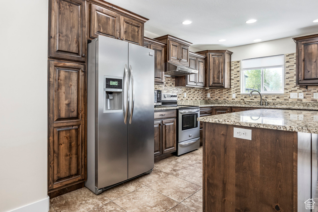 Kitchen featuring dark brown cabinets, backsplash, stainless steel appliances, and under cabinet range hood