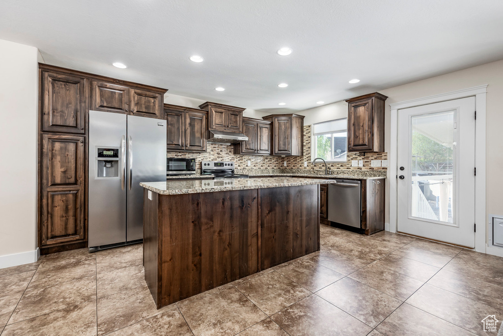 Kitchen with decorative backsplash, dark brown cabinetry, a kitchen island, under cabinet range hood, and stainless steel appliances