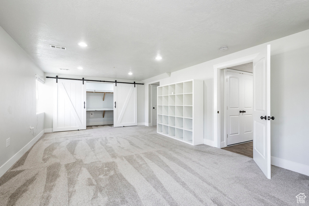 Interior space with visible vents, a barn door, baseboards, light carpet, and recessed lighting
