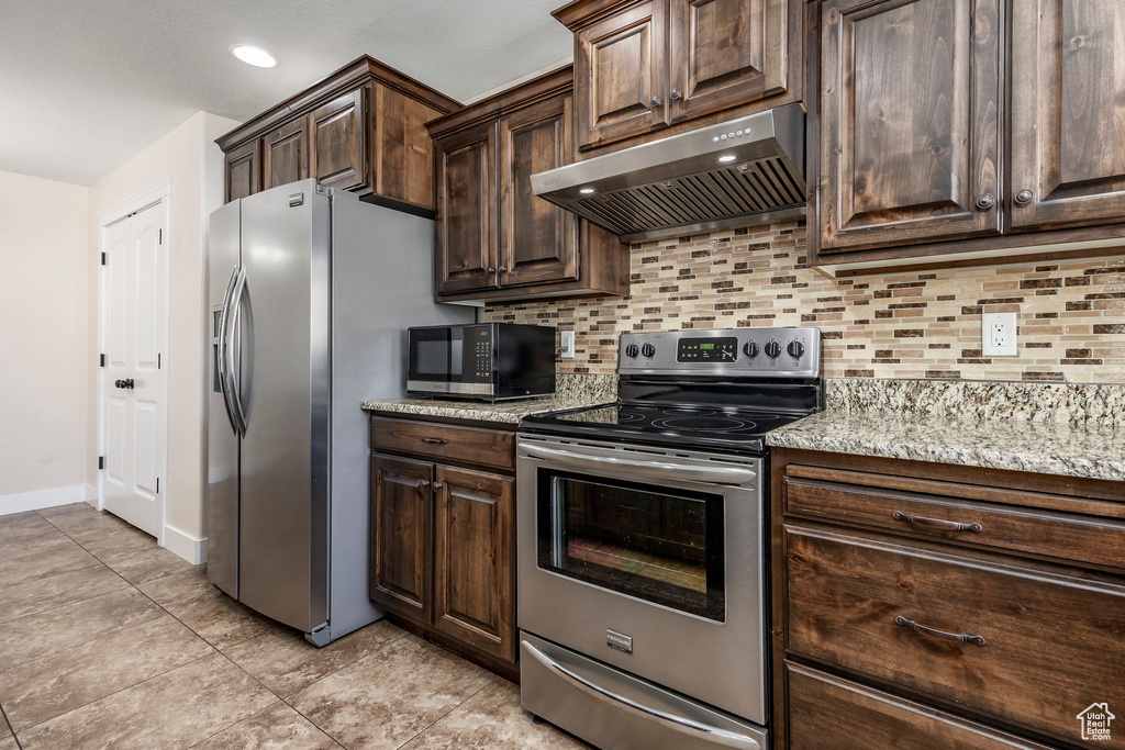 Kitchen with backsplash, appliances with stainless steel finishes, dark brown cabinets, baseboards, and ventilation hood