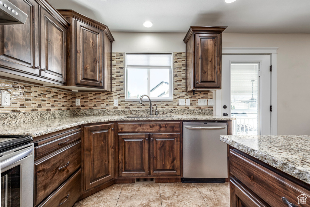 Kitchen featuring dark brown cabinets, light stone countertops, a sink, stainless steel appliances, and tasteful backsplash
