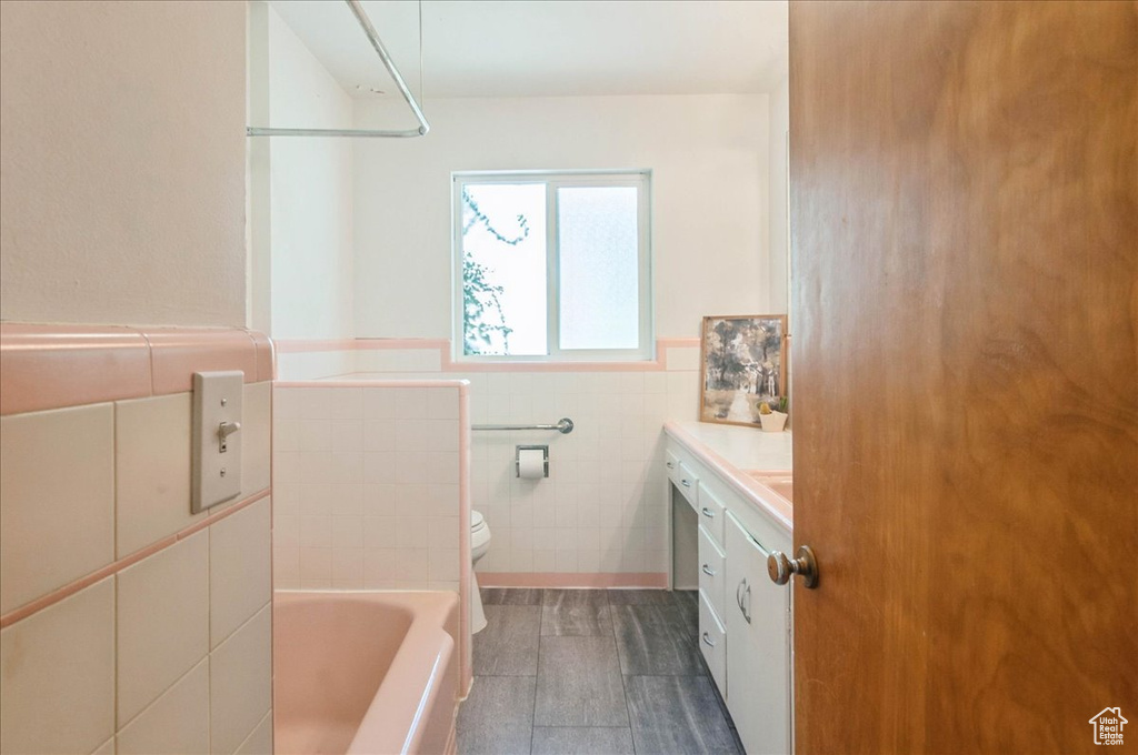 Bathroom featuring wainscoting, a bathing tub, toilet, tile walls, and wood finished floors