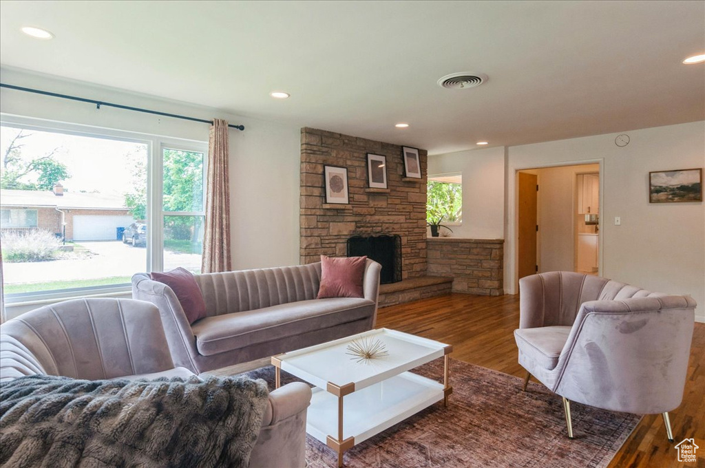 Living room featuring plenty of natural light, a stone fireplace, wood finished floors, and visible vents