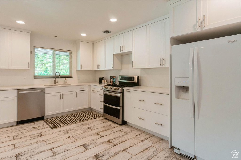 Kitchen featuring a sink, light wood finished floors, appliances with stainless steel finishes, and white cabinetry