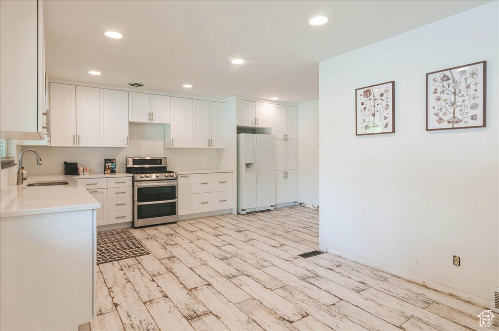 Kitchen featuring white refrigerator with ice dispenser, light countertops, a sink, light wood-style flooring, and double oven range