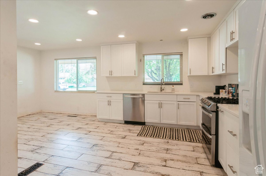 Kitchen featuring a sink, appliances with stainless steel finishes, white cabinetry, and a healthy amount of sunlight