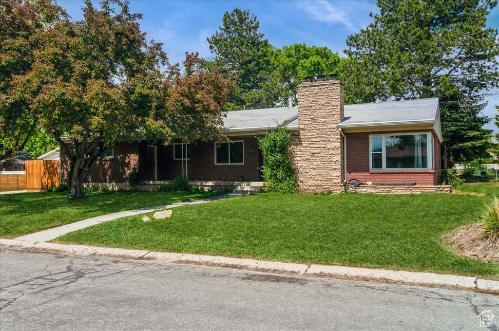 Single story home featuring fence, a chimney, a front lawn, and brick siding