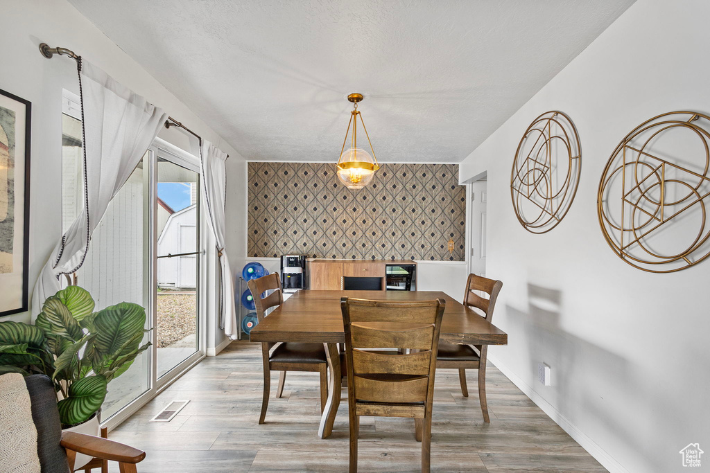 Dining space with visible vents, wood finished floors, an accent wall, baseboards, and wallpapered walls