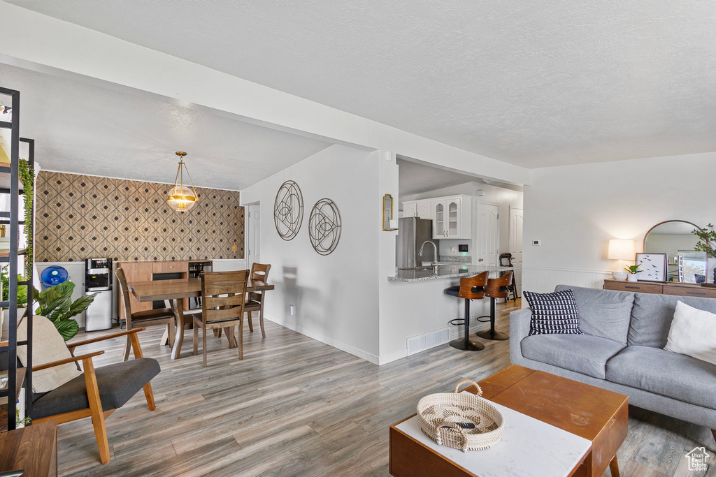 Living area with visible vents, an accent wall, baseboards, wallpapered walls, and light wood finished floors