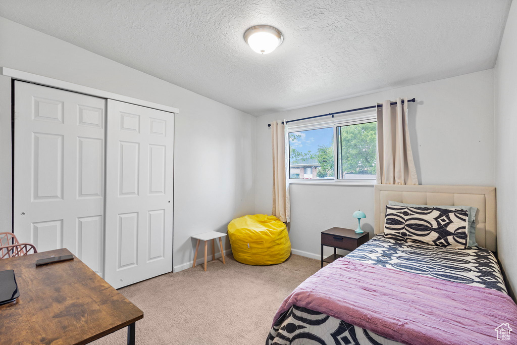 Carpeted bedroom with a closet, a textured ceiling, and baseboards