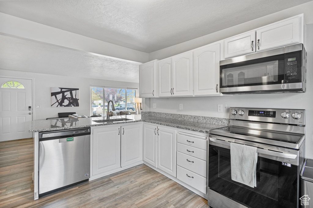 Kitchen featuring appliances with stainless steel finishes, light stone counters, a sink, light wood finished floors, and a textured ceiling