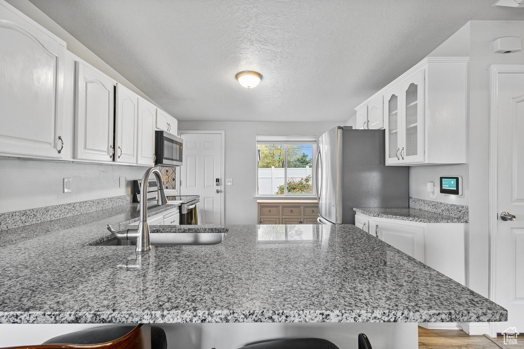 Kitchen featuring a breakfast bar, a sink, stainless steel appliances, a peninsula, and glass insert cabinets
