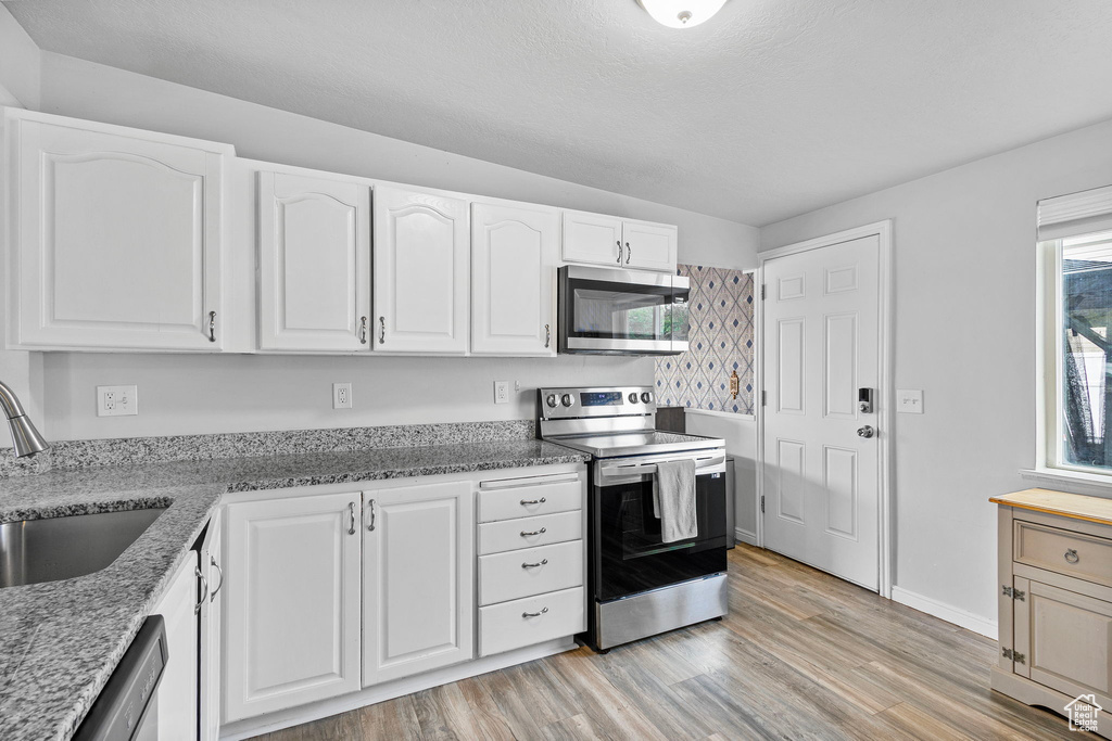 Kitchen featuring light stone countertops, appliances with stainless steel finishes, a sink, light wood-style flooring, and white cabinetry