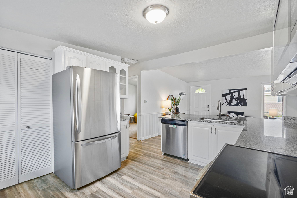 Kitchen with white cabinets, a sink, a textured ceiling, stone countertops, and stainless steel appliances