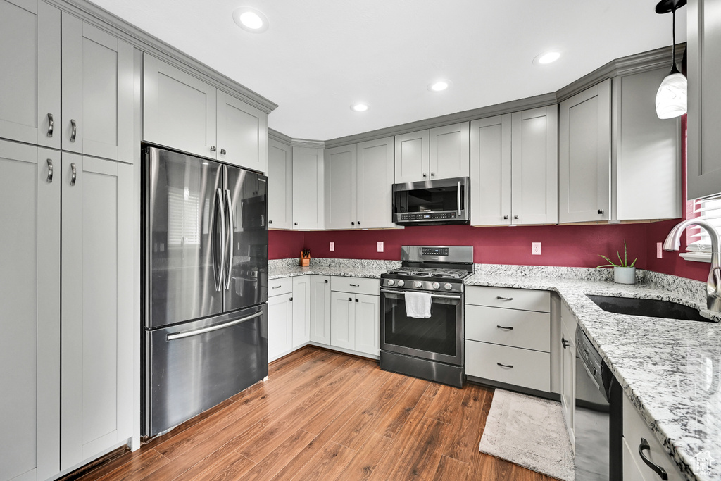 Kitchen with light stone countertops, appliances with stainless steel finishes, a sink, gray cabinets, and wood finished floors