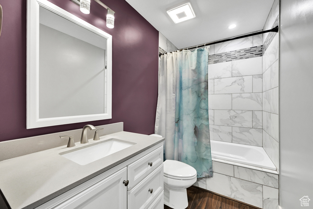 Bathroom with wood finished floors, vanity, tiled shower / bath, toilet, and recessed lighting