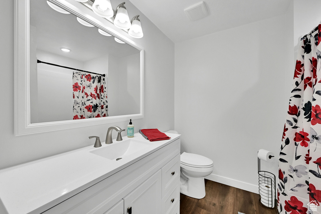 Full bath with visible vents, wood finished floors, vanity, baseboards, and toilet