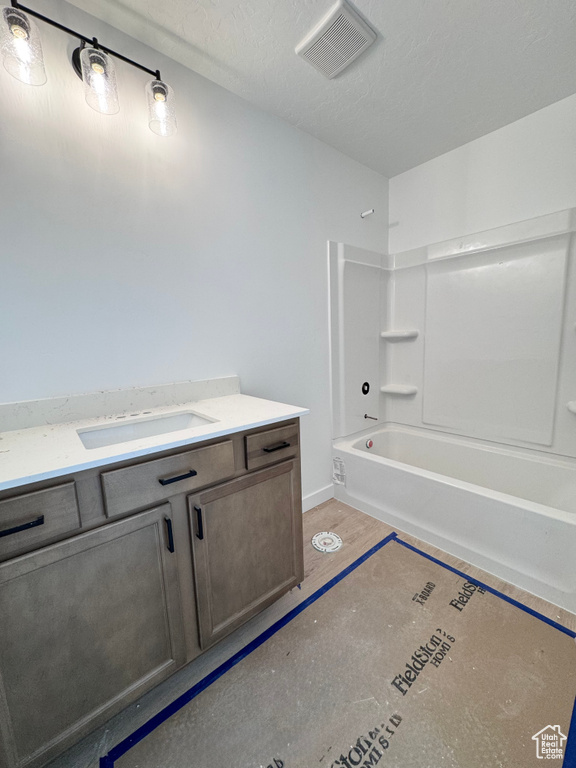 Bathroom featuring a textured ceiling, visible vents, vanity, baseboards, and washtub / shower combination