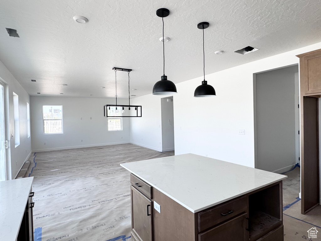 Kitchen with light countertops, a textured ceiling, light wood-style flooring, a kitchen island, and pendant lighting