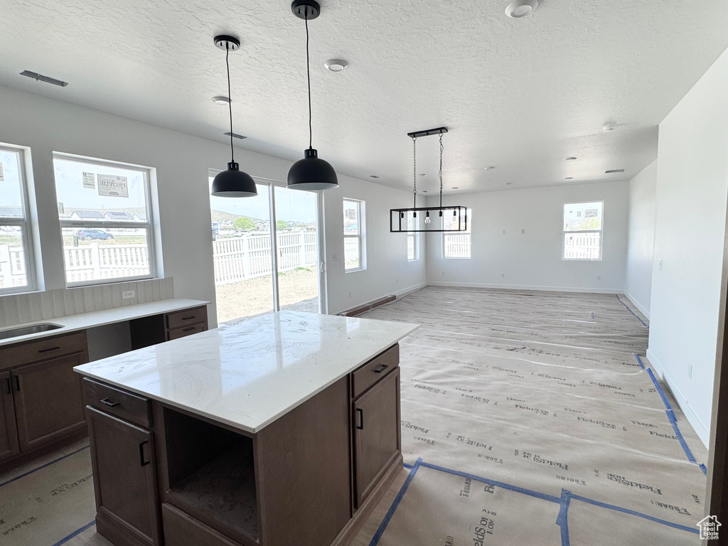 Kitchen with dark brown cabinetry, open floor plan, pendant lighting, and light wood-type flooring