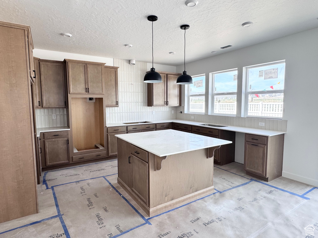 Kitchen featuring decorative backsplash, a textured ceiling, a center island, hanging light fixtures, and cooktop