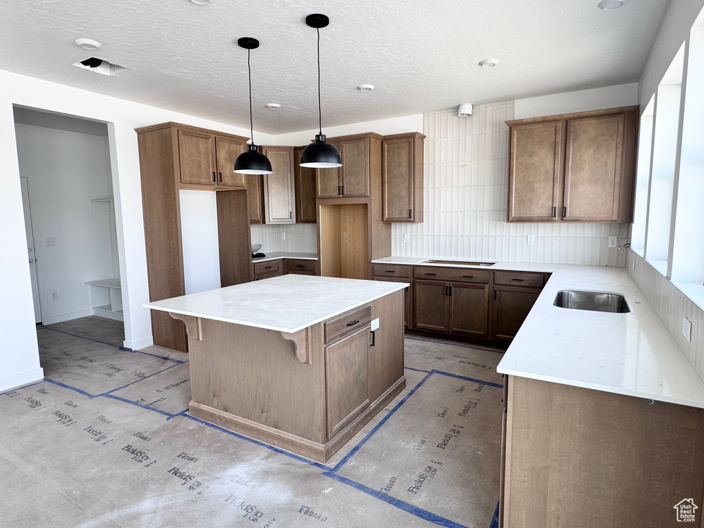 Kitchen with decorative backsplash, a kitchen island, a textured ceiling, pendant lighting, and brown cabinets