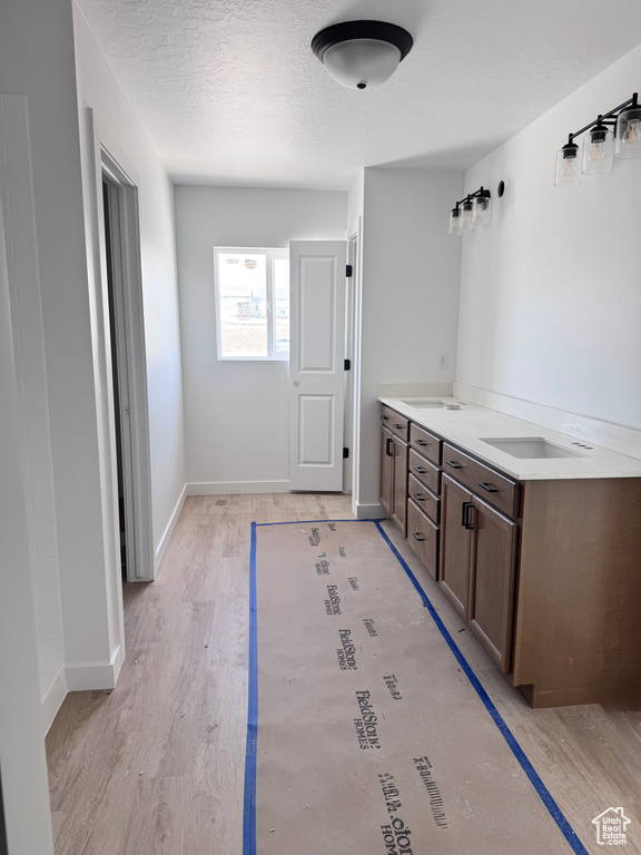 Bathroom with baseboards, double vanity, a textured ceiling, and wood finished floors