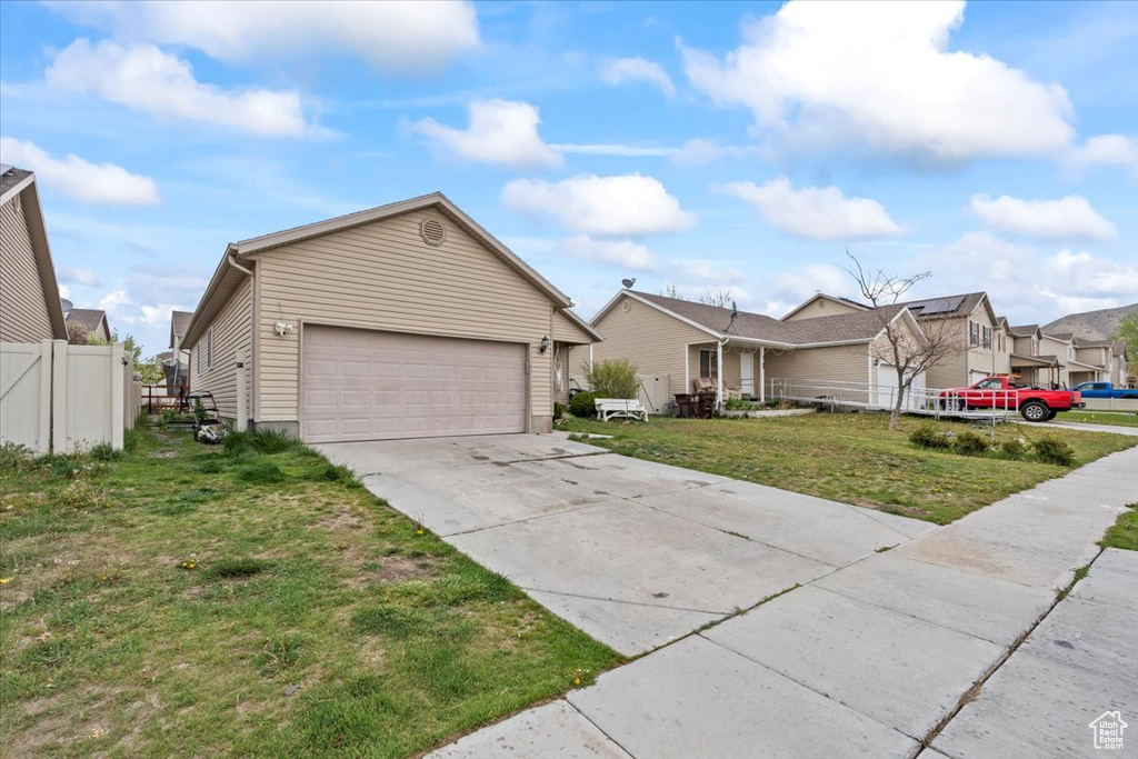 Ranch-style home with driveway, a front yard, a residential view, fence, and an attached garage