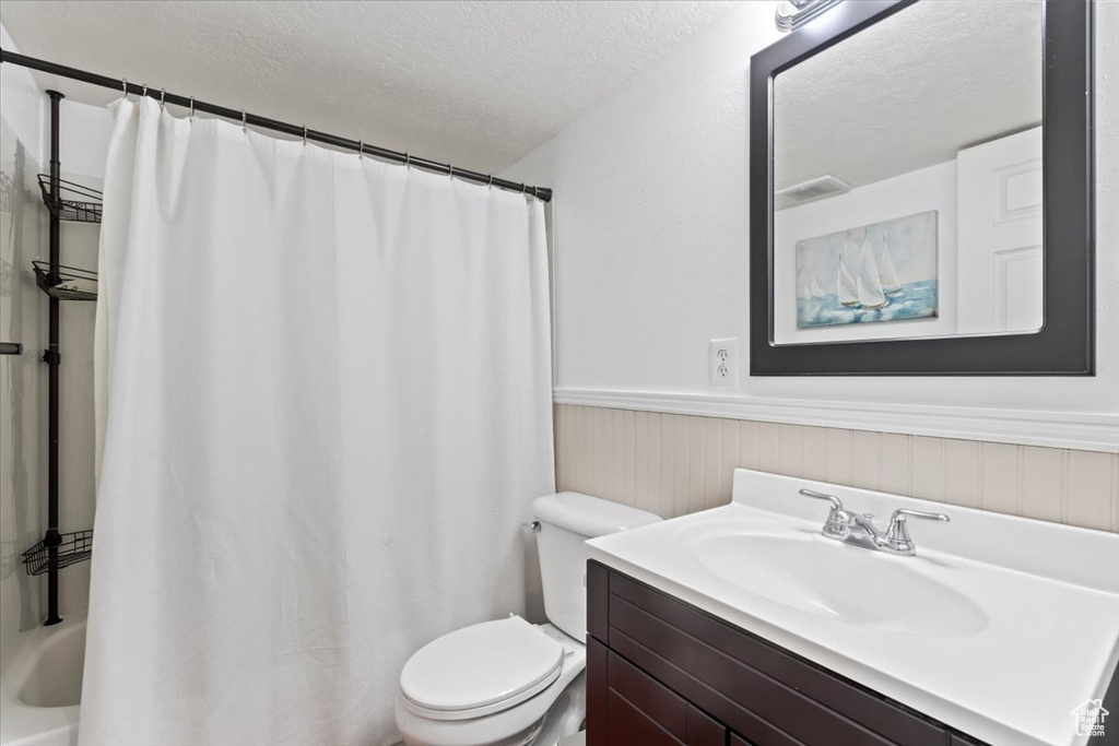Full bath featuring toilet, a textured ceiling, wainscoting, and vanity