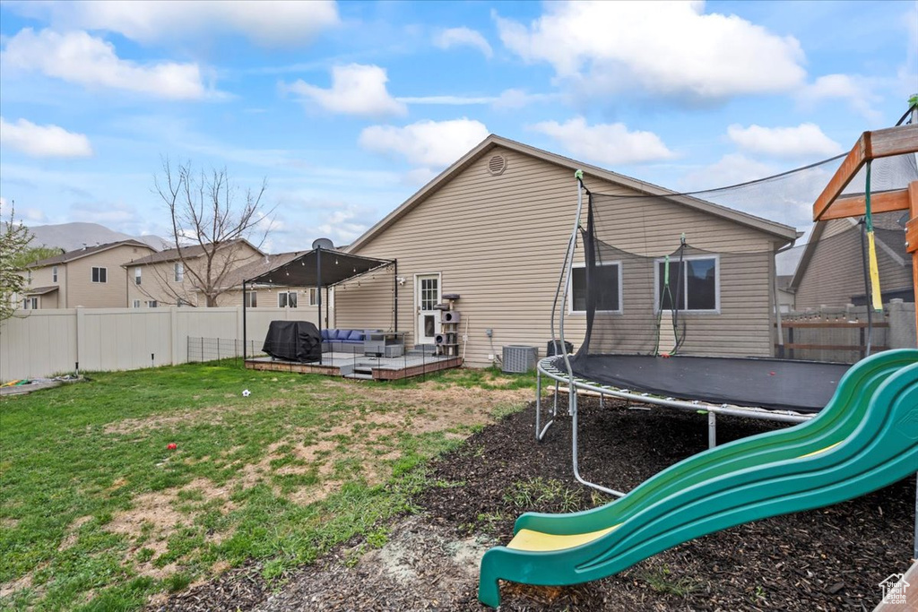 Back of house featuring a trampoline, a lawn, a fenced backyard, an outdoor hangout area, and a patio