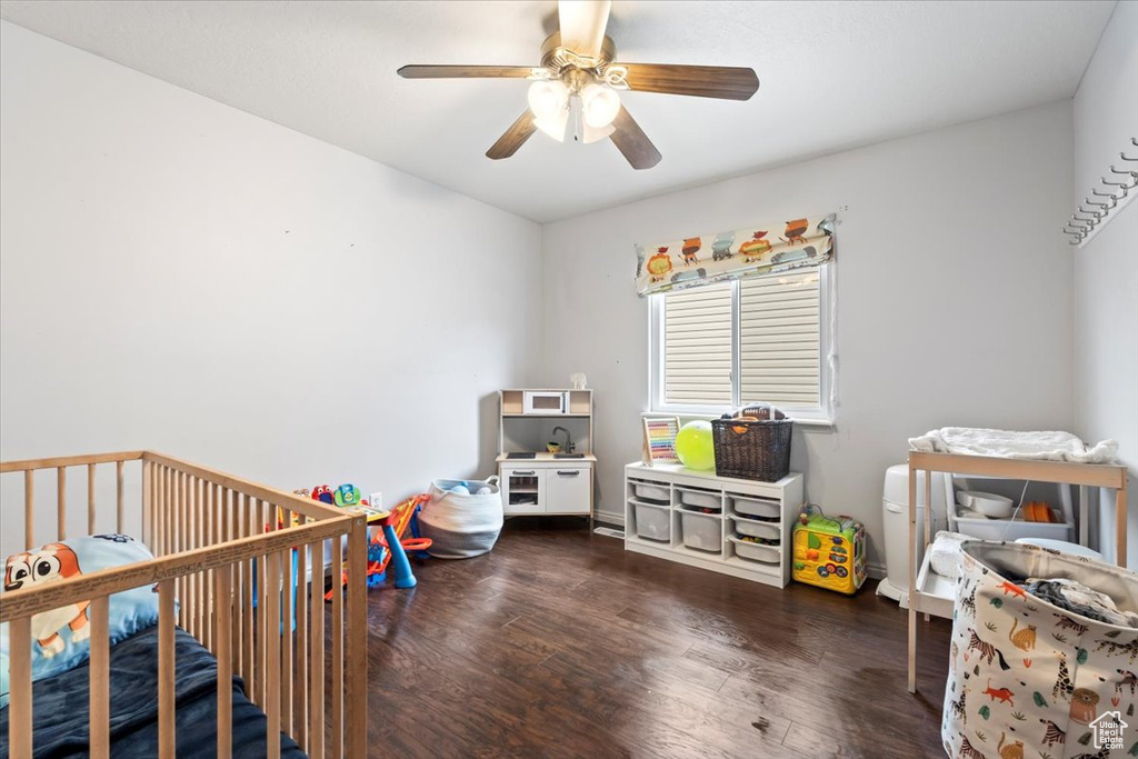 Bedroom with a nursery area, a ceiling fan, and wood finished floors