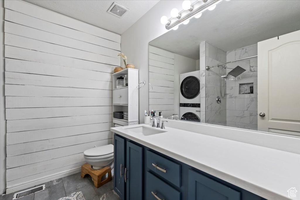 Bathroom featuring visible vents, stacked washer / drying machine, vanity, toilet, and tiled shower