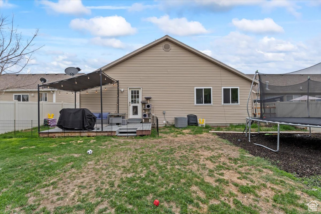 Rear view of house with fence, a trampoline, central AC, outdoor lounge area, and a lawn