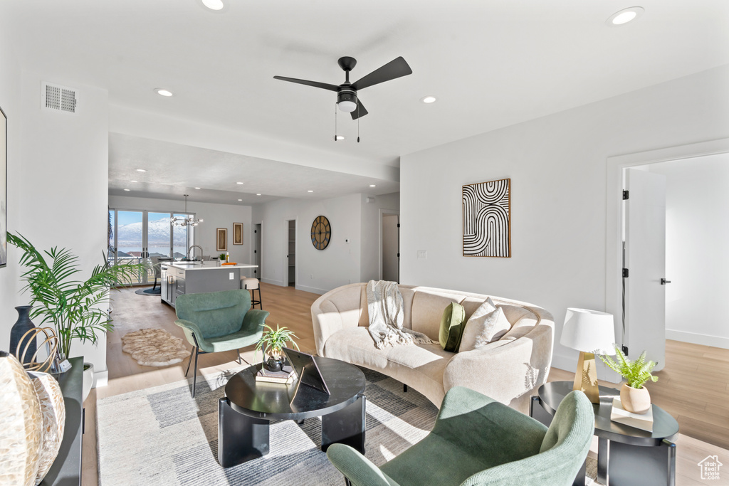 Living room featuring light wood finished floors, ceiling fan with notable chandelier, recessed lighting, and visible vents
