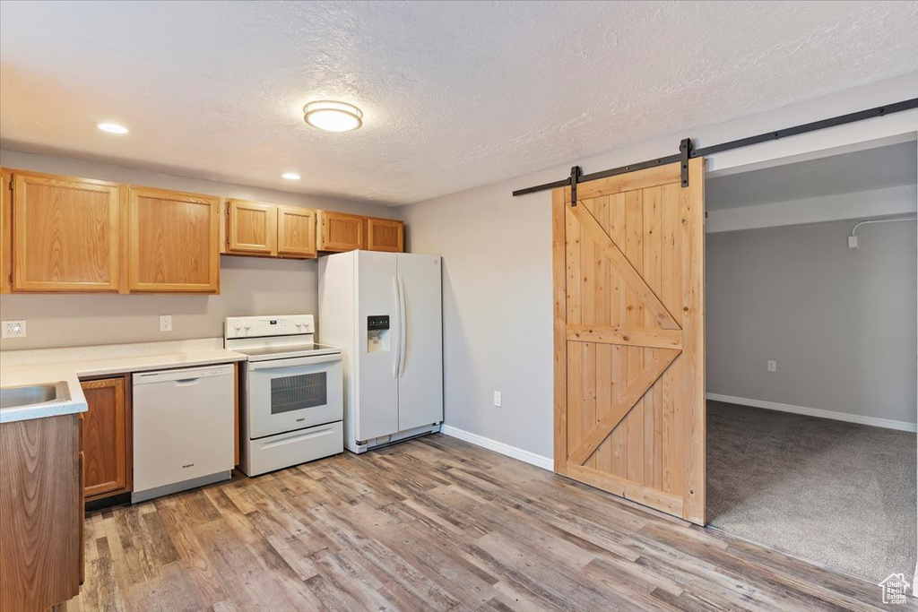 Kitchen featuring white appliances, a barn door, light countertops, light wood-type flooring, and recessed lighting
