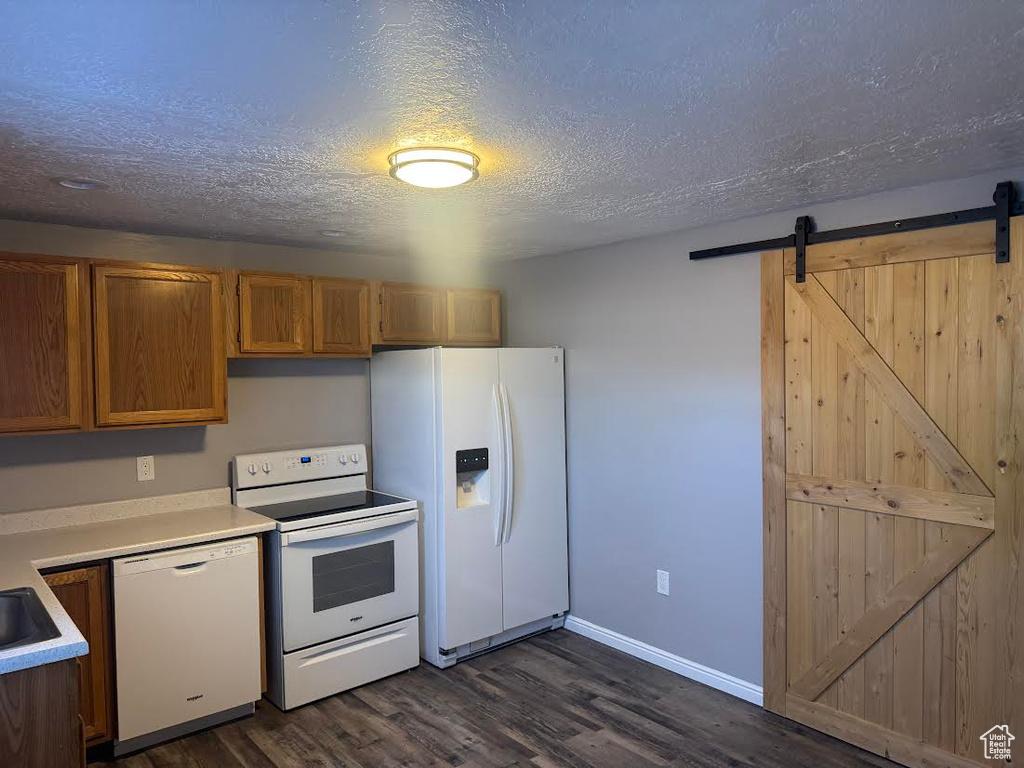Kitchen with white appliances, dark wood-type flooring, a barn door, a textured ceiling, and light countertops