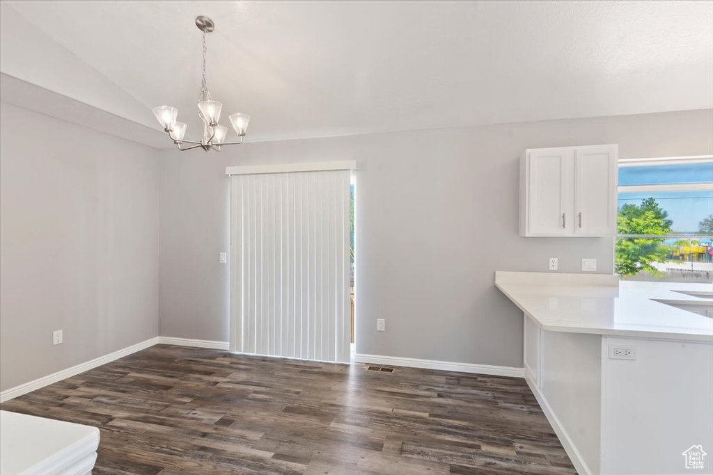 Unfurnished dining area with dark wood finished floors, a chandelier, baseboards, and vaulted ceiling