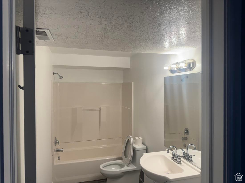 Full bathroom with washtub / shower combination, a sink, toilet, a textured ceiling, and visible vents