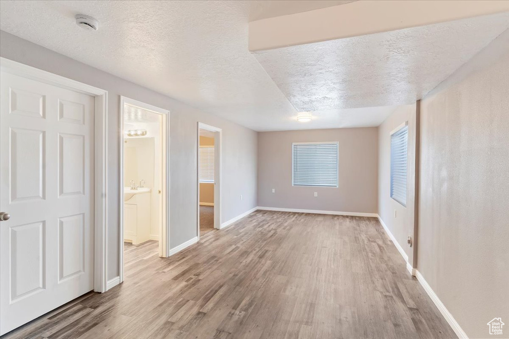 Unfurnished bedroom with light wood-style flooring, a textured ceiling, baseboards, and ensuite bath