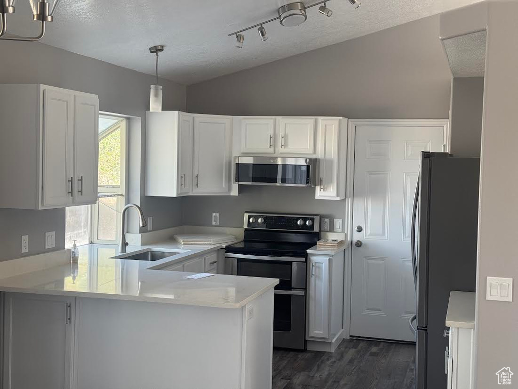 Kitchen with dark wood-style flooring, appliances with stainless steel finishes, a sink, a peninsula, and white cabinetry